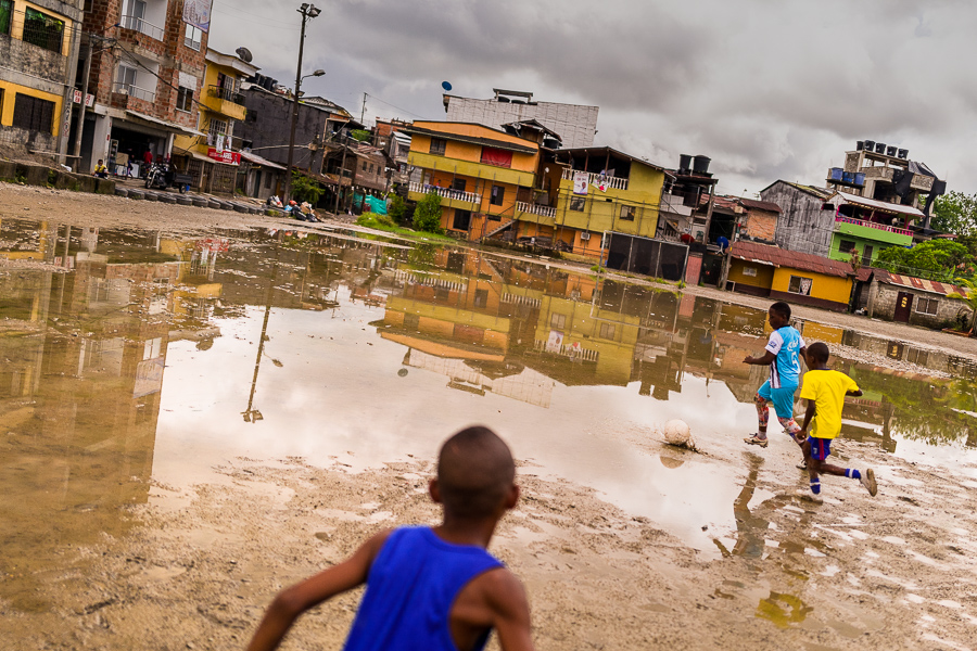 Young Afro-Colombian football players compete for the ball during a training session on a dirt playing field in Quibdó, Chocó, Colombia.