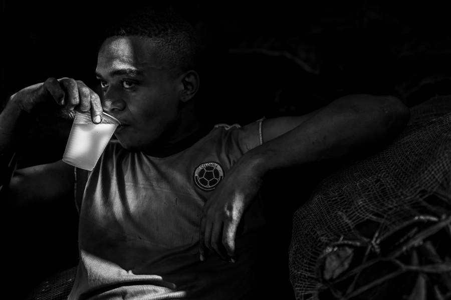 An Afro-Colombian charcoal worker drinks cold milk during his work break while hidden in the shadow at the street market in Cartagena, Colombia.