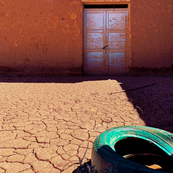 A painted tire lies on the dry, cracked soil in front of the entrance to a house in the desert of San Juan Province, Argentina.