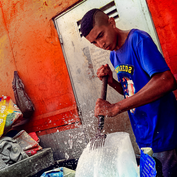 A young Afro-Colombian man crushes a block of ice for fresh fish sold in the street market in Barranquilla, Colombia.