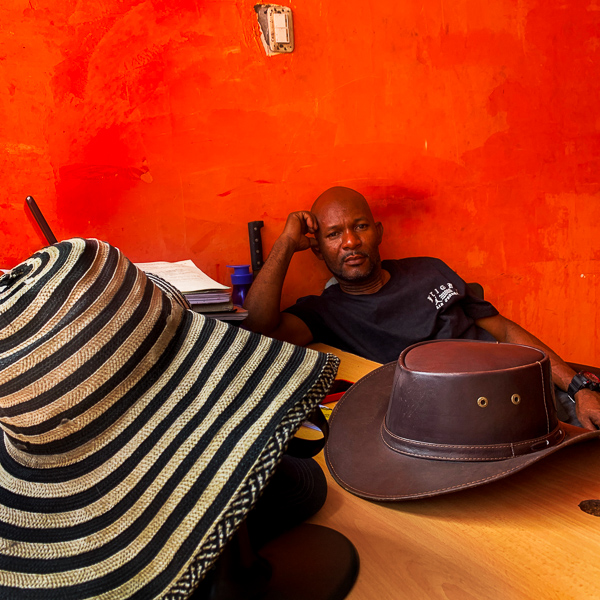 A Colombian man sits at a table with a traditional Colombian sombrero vueltiao placed on it, in a street shop in Cali, Colombia.