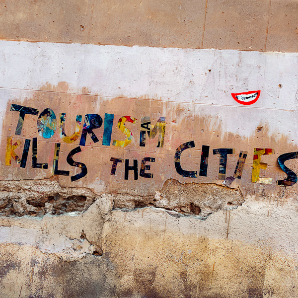 A typographic artwork depicting the statement 'Tourism kills the cities' is seen glued on a wall in the street of Barcelona, Spain.