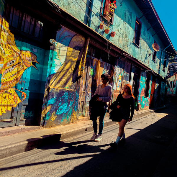 Young Chilean students walk down a narrow street decorated with graffiti artworks on Cerro Concepción hill in Valparaíso, Chile.